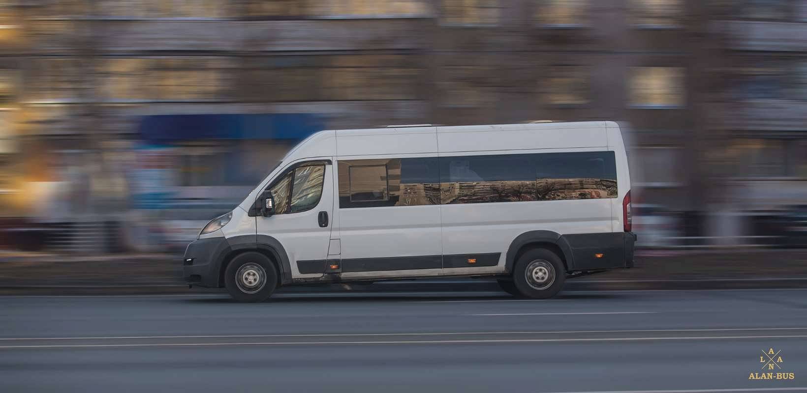 Biały bus ALAN-BUS w ruchu, poruszający się ulicą na tle miejskiej zabudowy.jpg