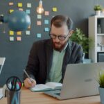 Man working at desk with laptop and notebook.