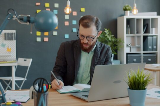 Man working at desk with laptop and notebook.